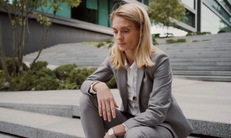 devojka u sivom odelu i beloj košulji sedi na stepenicama