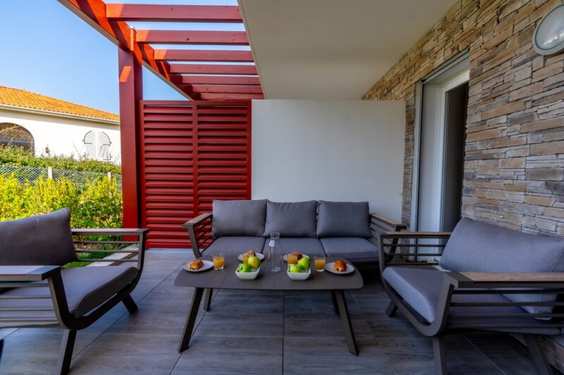 Uređena terasa sa sivom garniturom za sedenje, niskim stočićem i dekorativnim kamenim zidom, pogodna za opuštanje i druženje