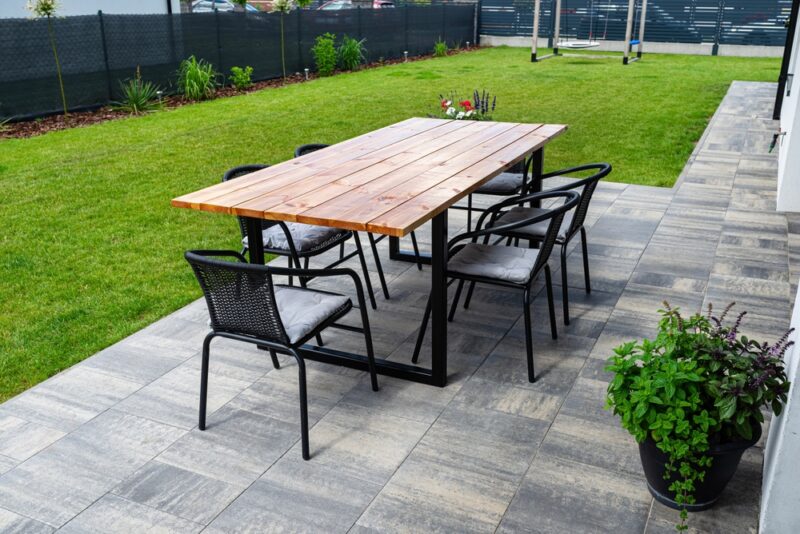 Terasa sa sivim keramičkim pločama, drvenim stolom i stolicama u uređenom dvorištu